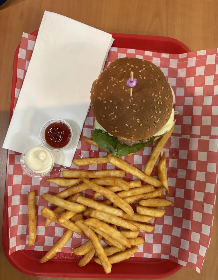 A sesame-bun burger with a pile of fries and two sauces on a red tray