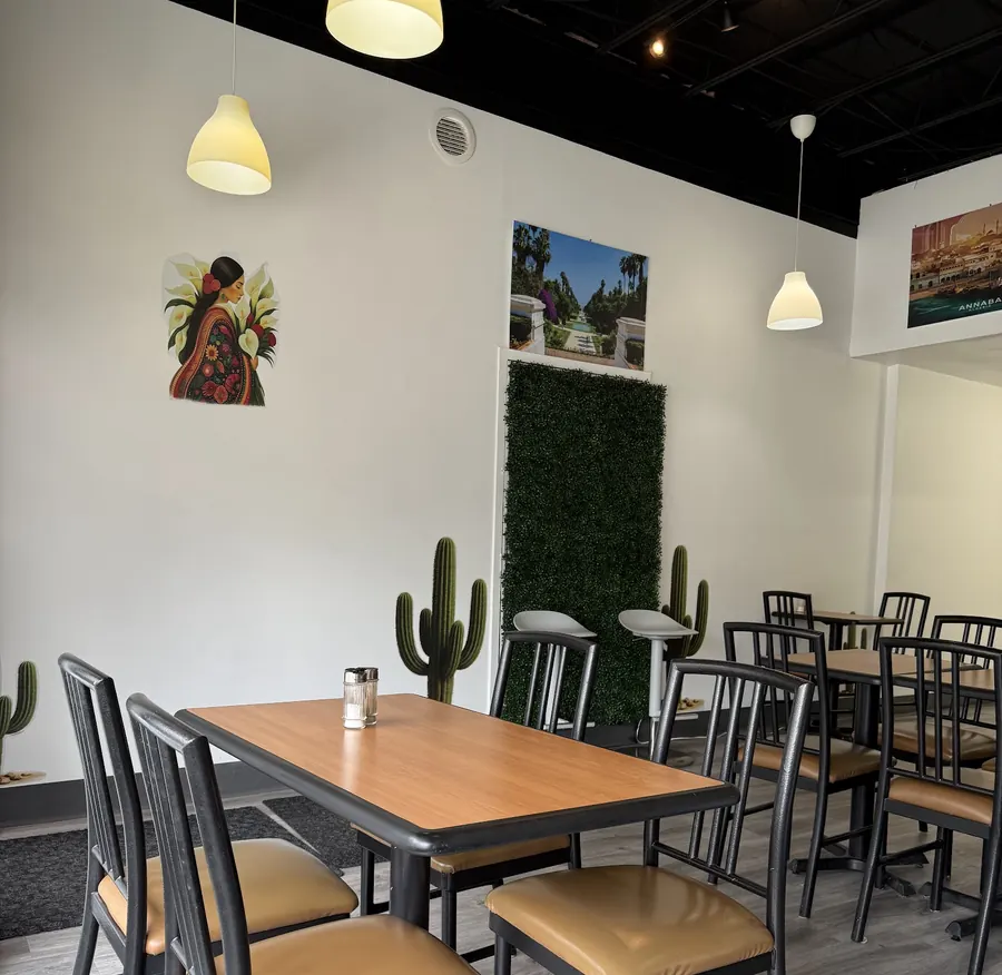 The dining room: wood-top tables, black chairs with tan seats, a green hedge wall and two cactus decorations