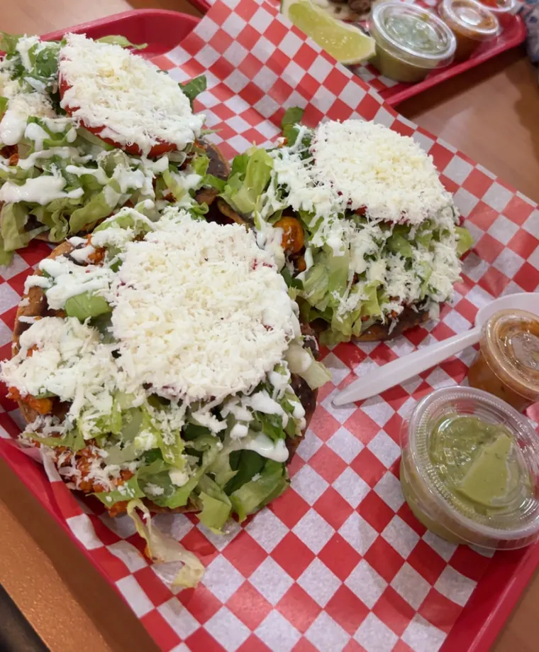 Tostadas piled with shredded lettuce, crumbled white cheese and cream on a red tray